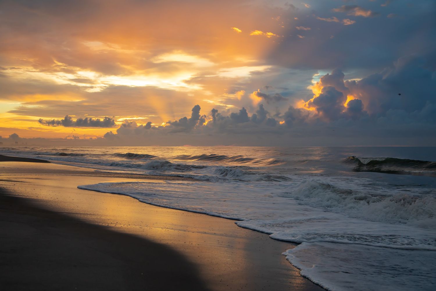 Dramatic orange sunset over ocean waves crashing on dark sandy beach.