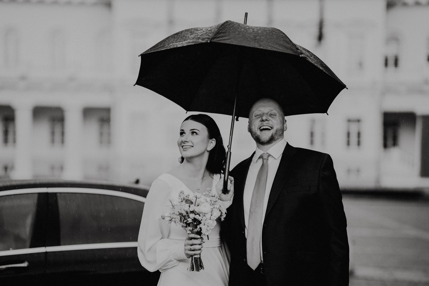 Wedding couple sharing intimate moments under black umbrellas in the rain.