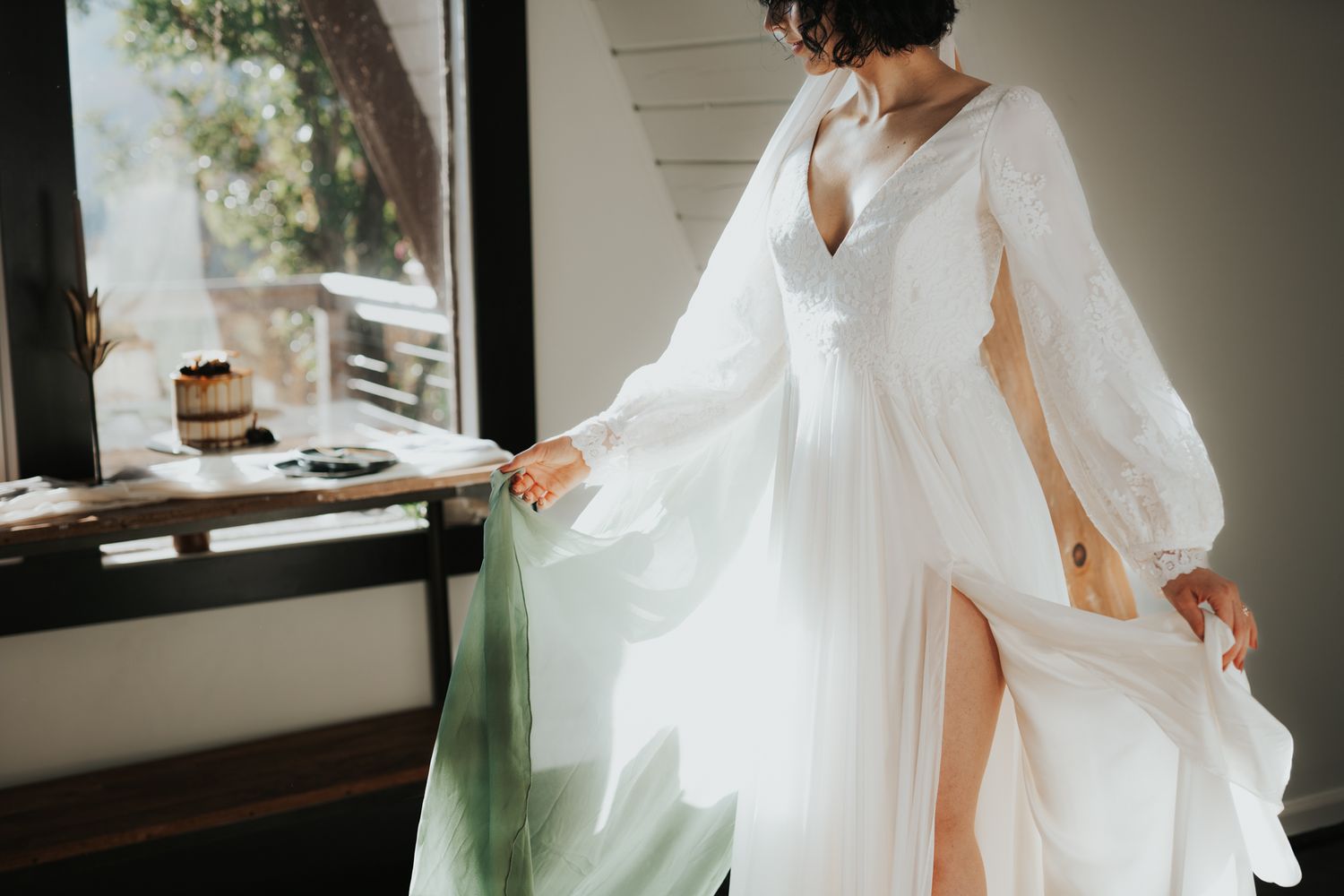 Bride in flowing white dress with billowing sleeves twirling by window.