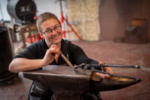 Craftsperson works at traditional anvil in rustic workshop setting.
