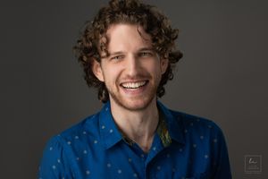 Portrait of person in blue polka dot shirt against dark background.