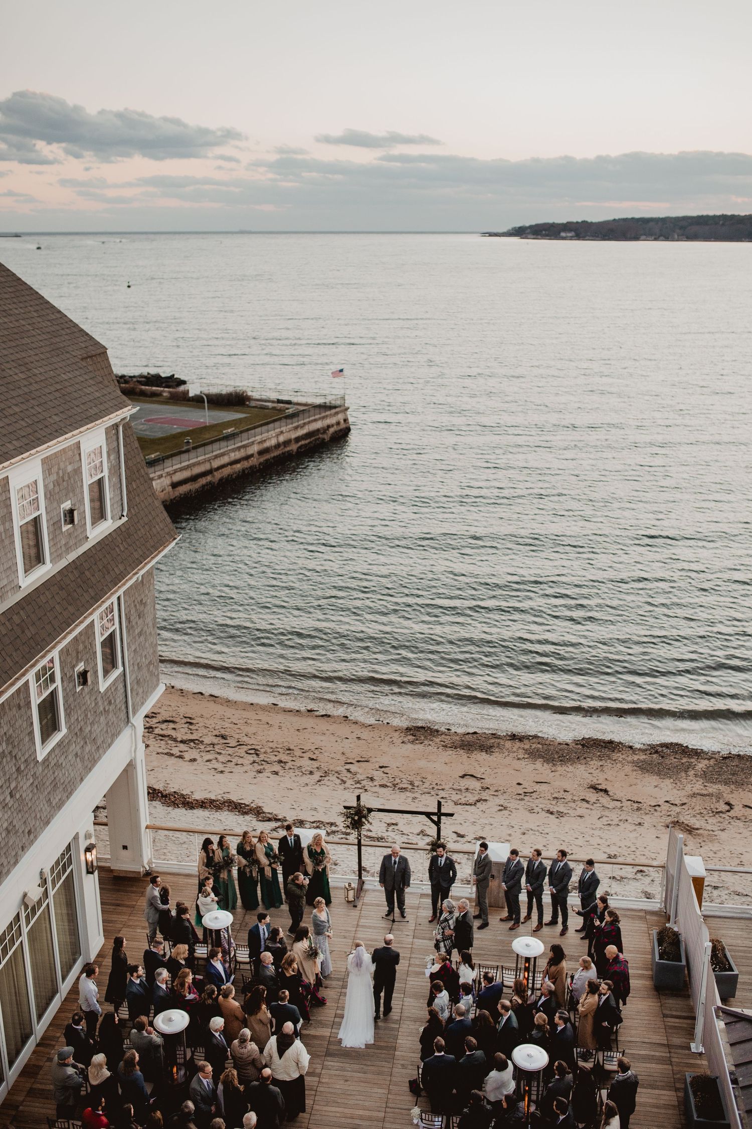 Aerial view of a seaside wedding ceremony with guests gathered on a beach deck.