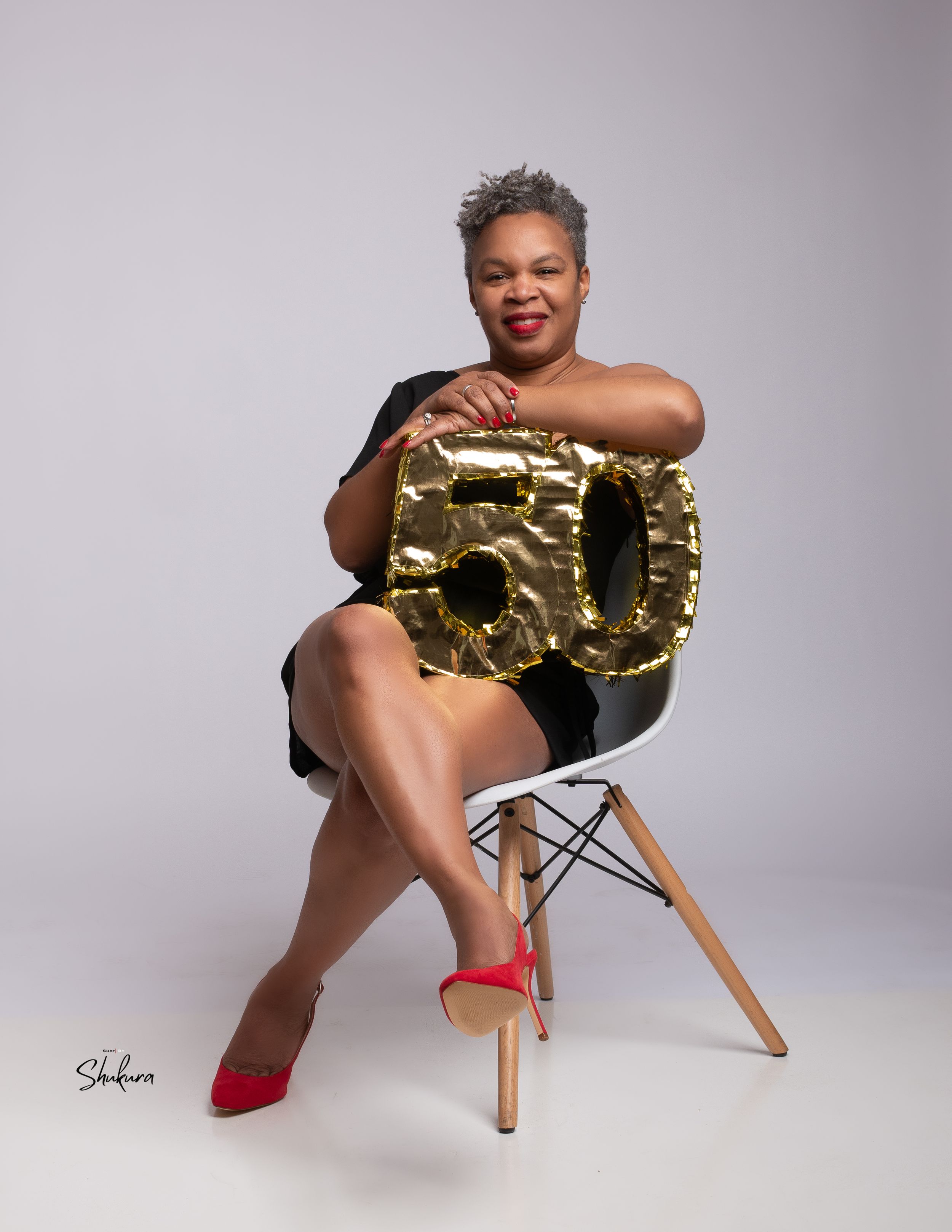 Studio portrait with gold number 50 prop on modern chair.