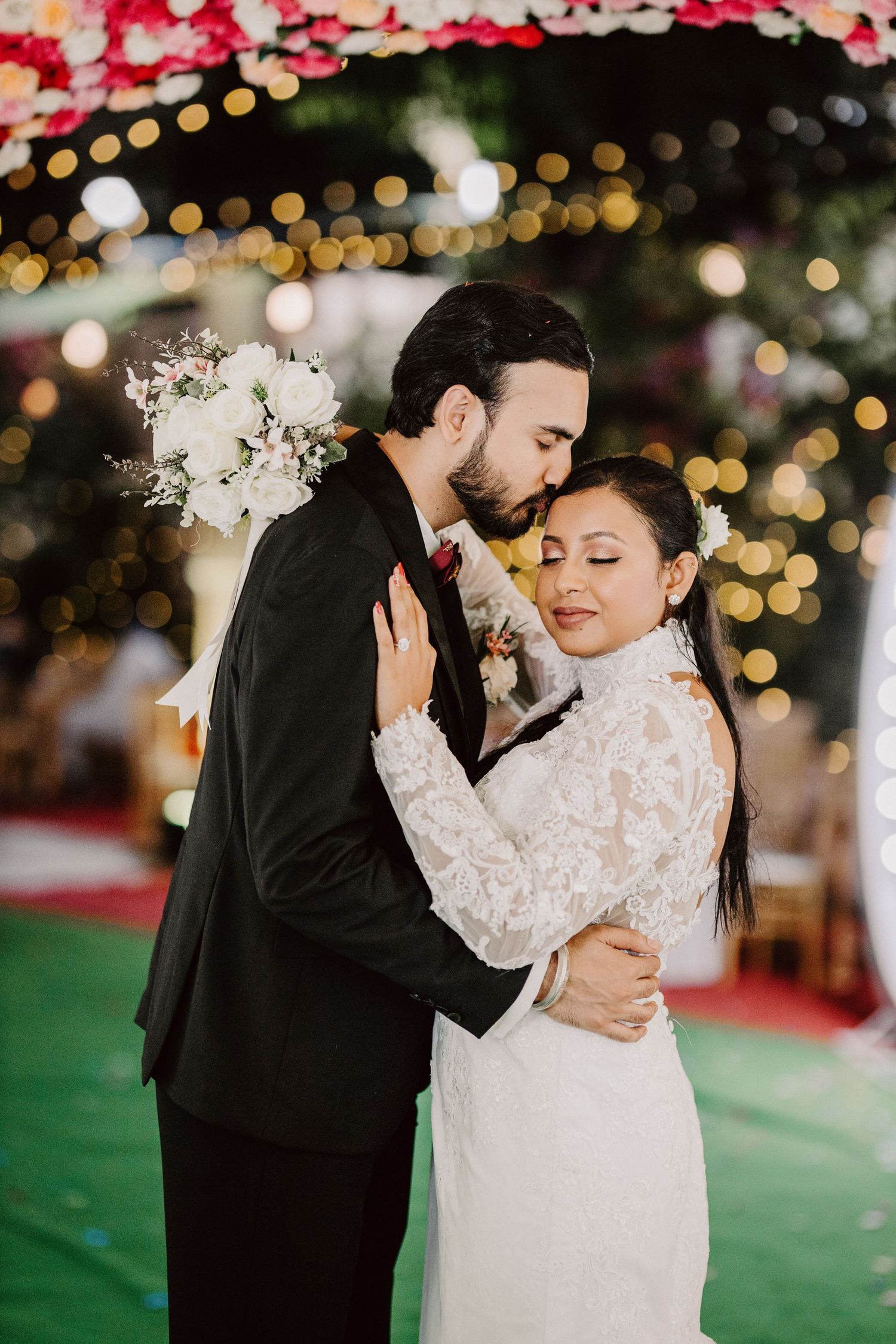 Intimate wedding moment captured with bokeh lights and floral decorations in the background.