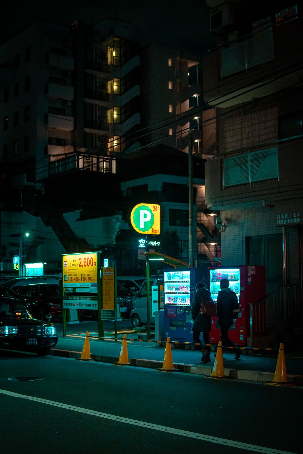 Urban street scene with parking sign and vending machines glowing in neon green light.