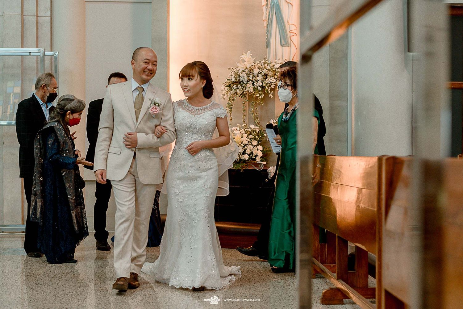 A bride and groom walk down a hallway decorated with elegant floral arrangements.