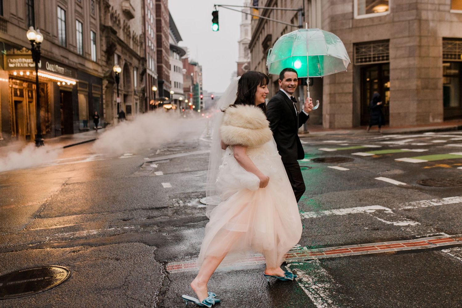 A couple dressed in wedding attire walks across a city street.