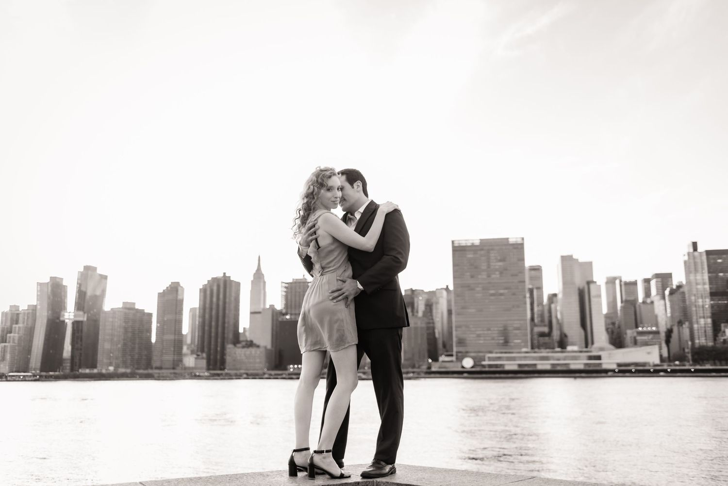 Black and white portrait of couple embracing with New York City skyline behind them.