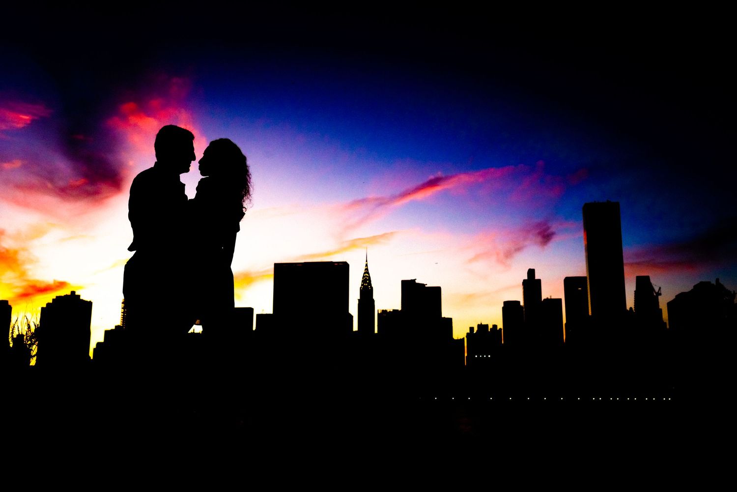 Silhouetted couple against a dramatic sunset with city skyline backdrop.