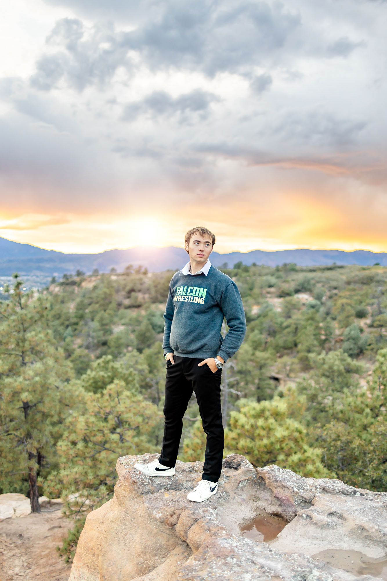 Senior guy in wrestling sweatshirt poses with hands in pockets at his senior session at Palmer Park in Colorado Springs.