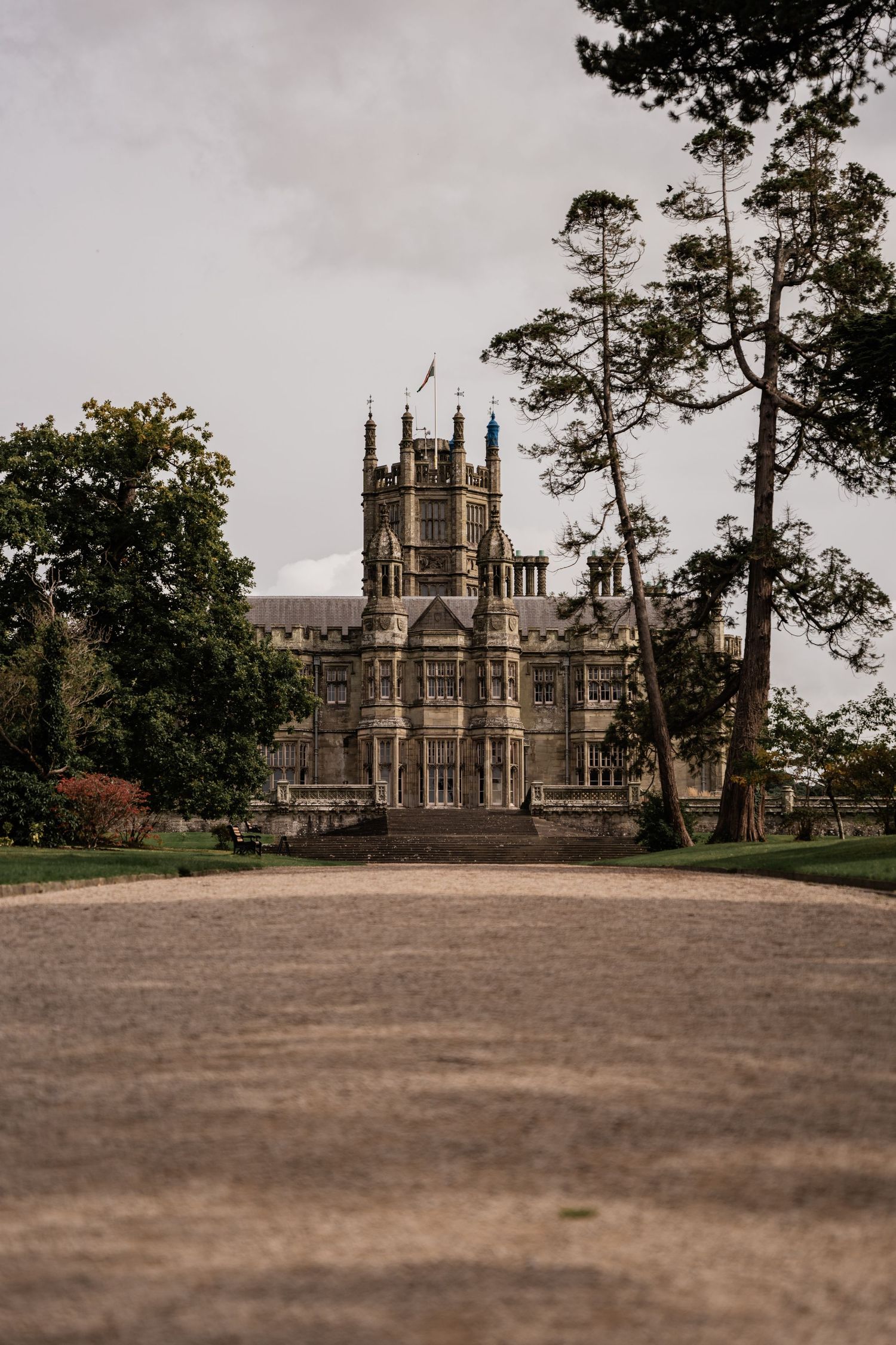 Gothic revival style castle with towering spires viewed through trees on an overcast day.