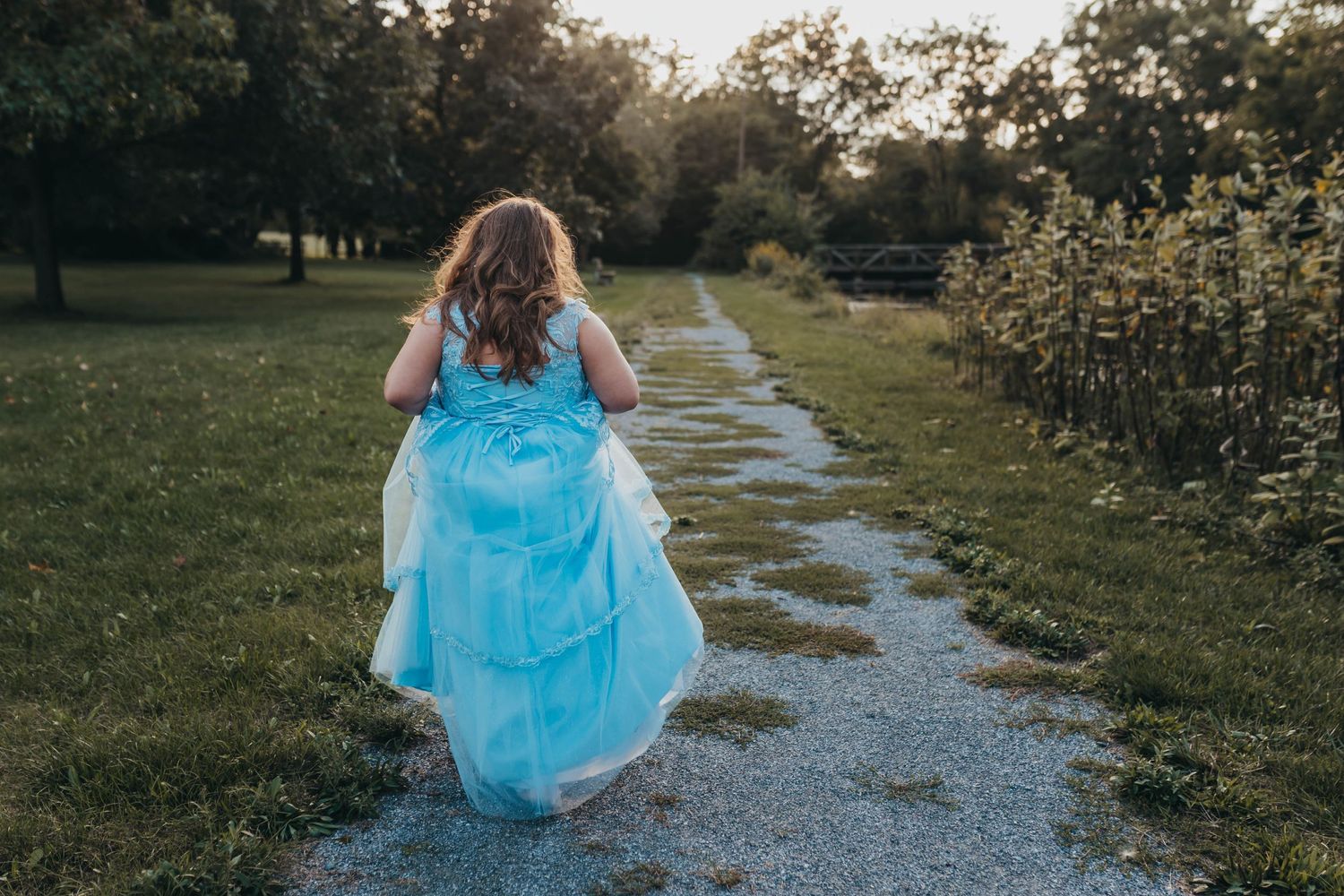 A person in a flowing blue dress runs down a garden path.