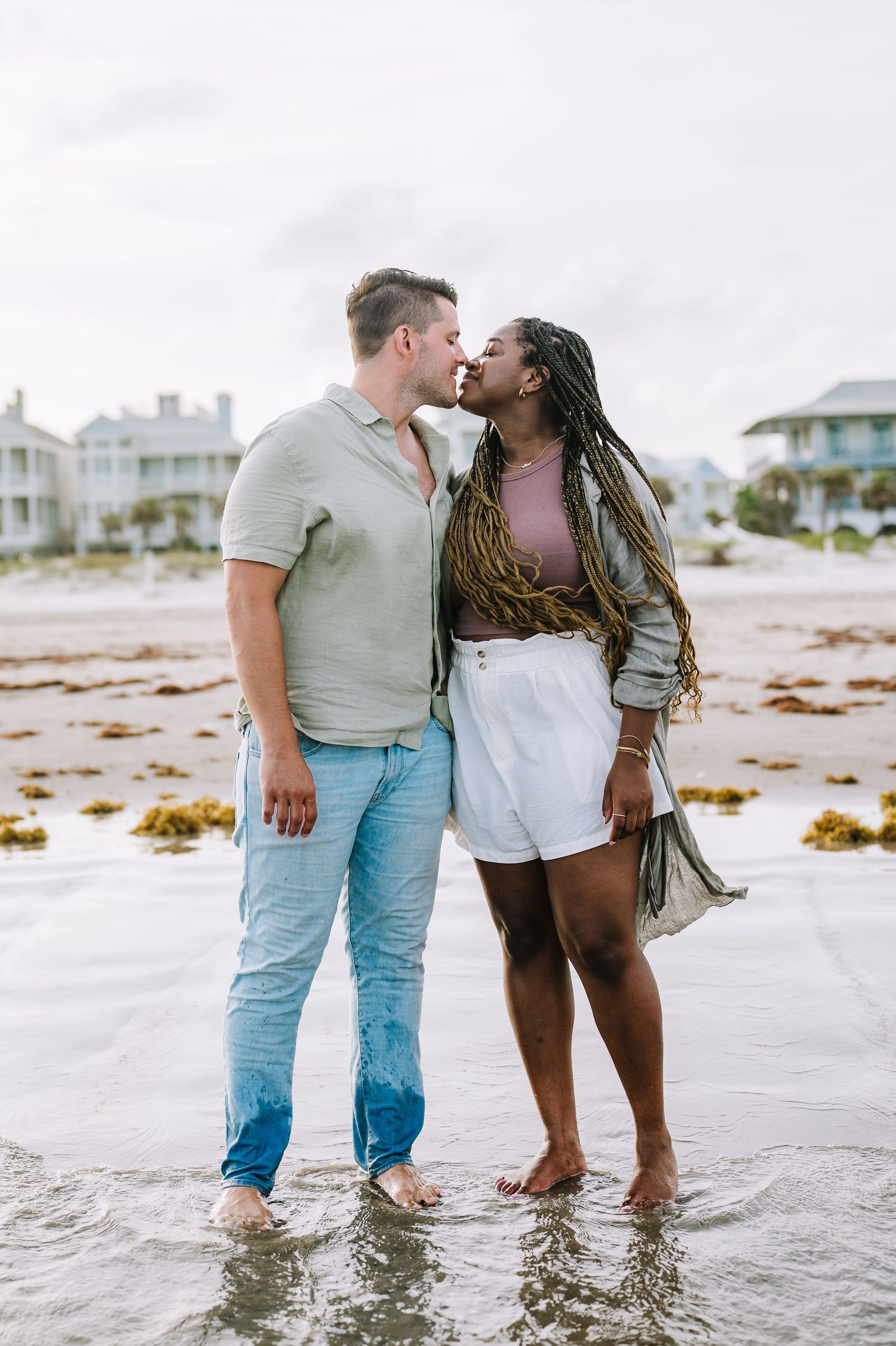 Romantic couple sharing tender moment while standing in ocean waves during beach photoshoot.