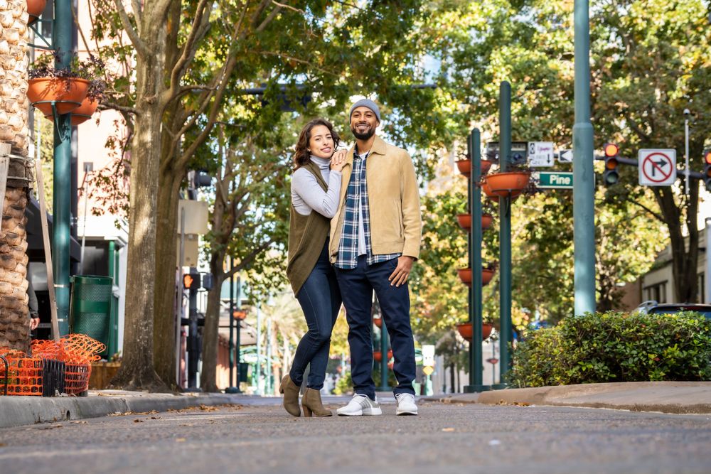 A couple stands together on a scenic urban street lined with autumn trees.