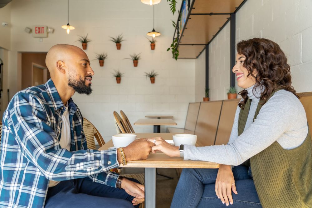 A couple talks while sitting at a cafe table with decorative wall fixtures.