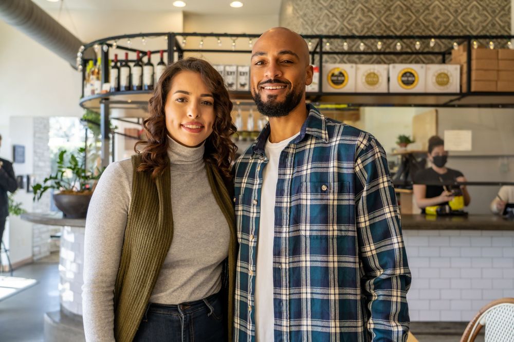 A couple smiles together inside a modern cafe with white tile walls.