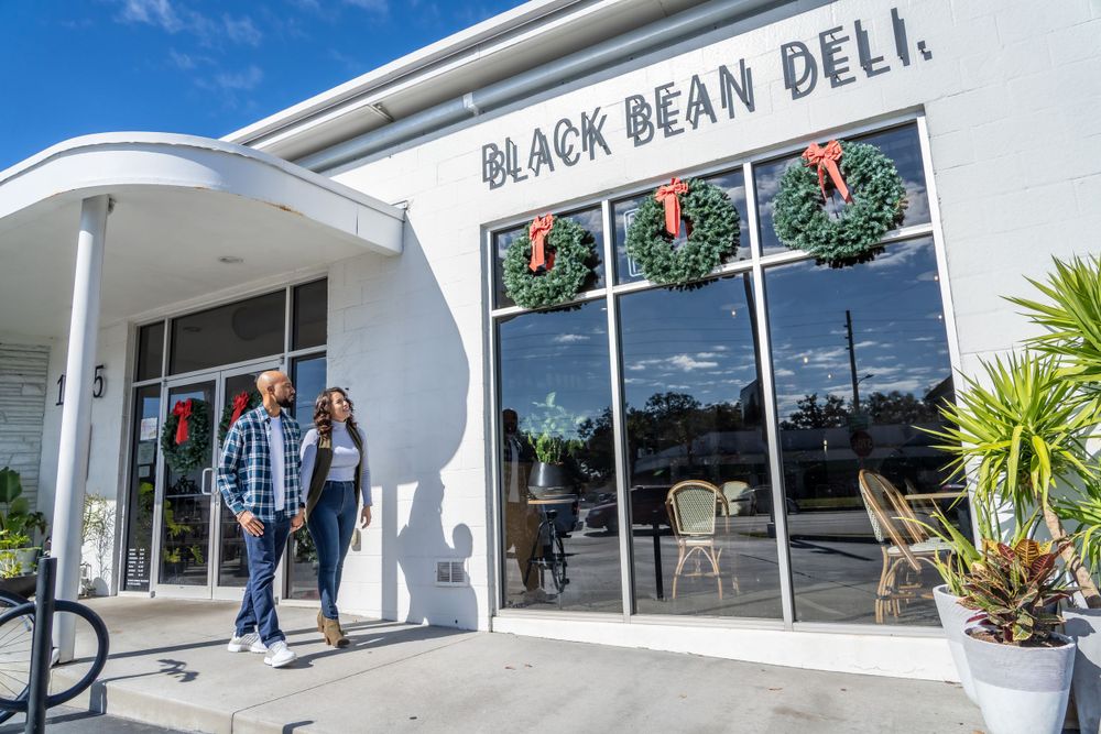 A couple walks outside Black Bean Deli with holiday wreaths in the windows.