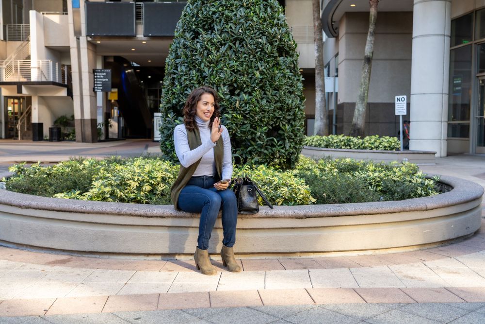 Person sitting on curved stone bench near landscaped garden and building entrance.
