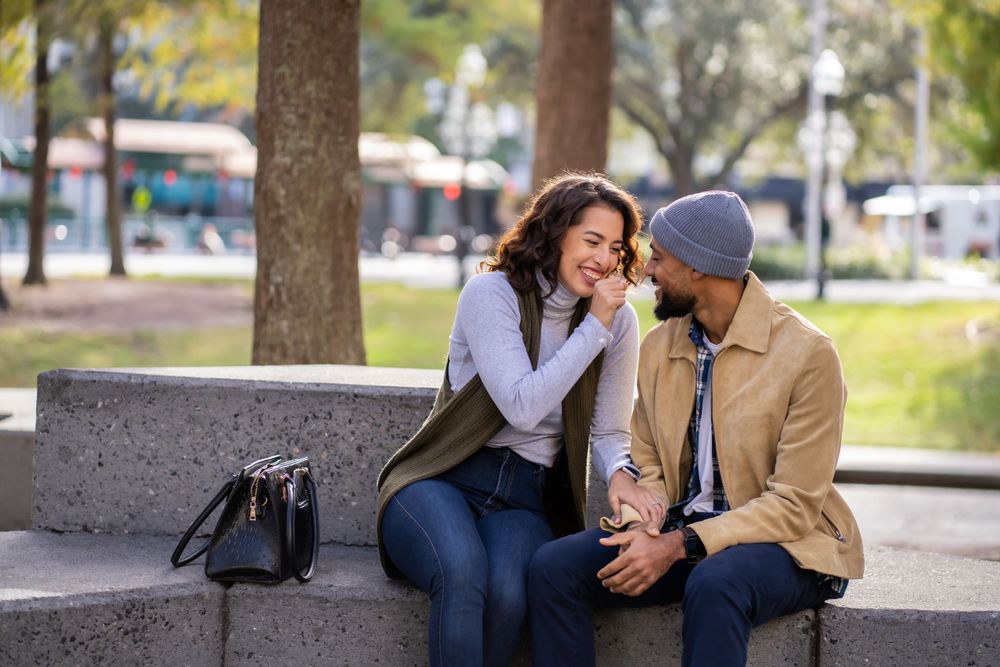 Couple sharing intimate moment while sitting on concrete bench in park.