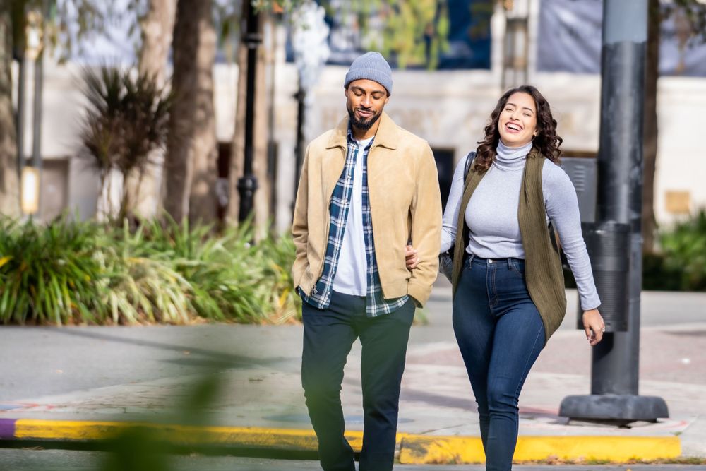 Couple walking together on sidewalk wearing casual fall outfits.