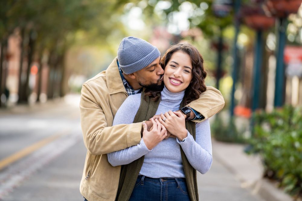 A couple shares an intimate embrace on a tree-lined street during autumn.