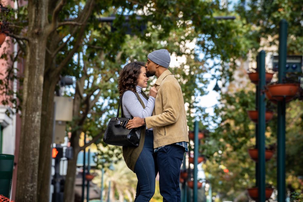 A romantic couple laughs together while standing on a city sidewalk.