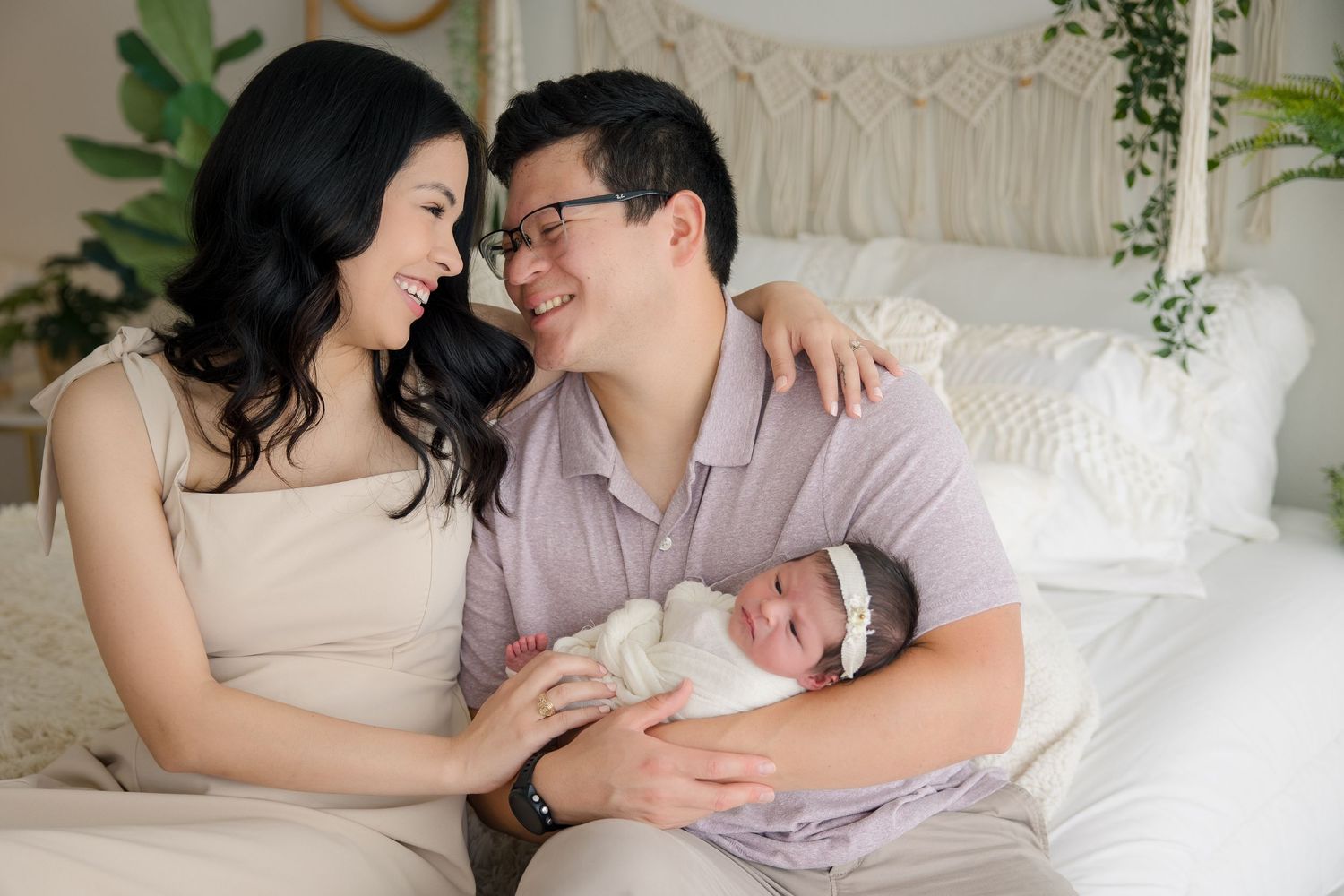 Family portrait with newborn baby in a bright, cozy bedroom setting.