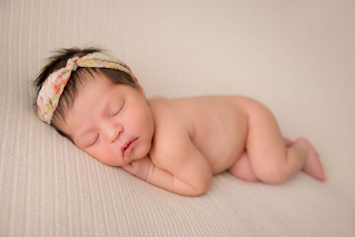 Newborn baby sleeping peacefully with delicate lace headband on cream backdrop.