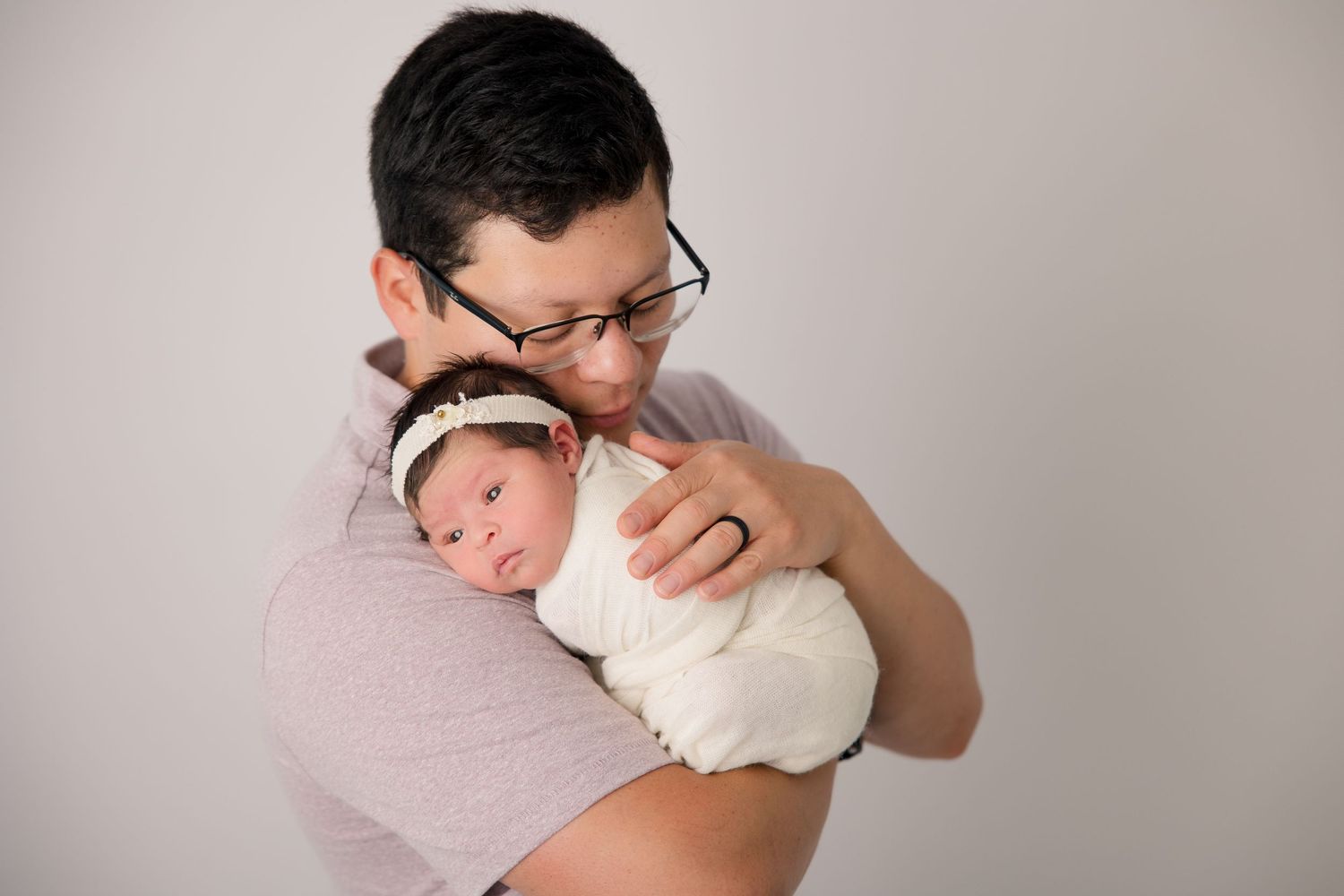 Parent in pink shirt embracing sleeping newborn in white wrap.