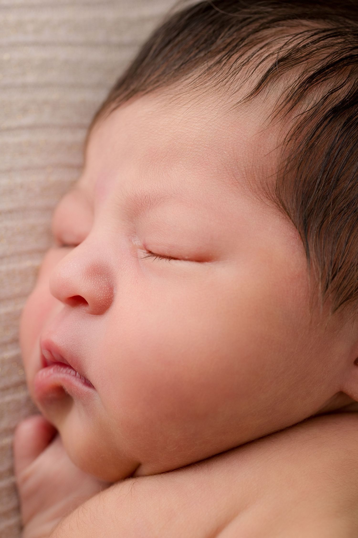 Close-up portrait of peaceful sleeping newborn baby against soft textured background.