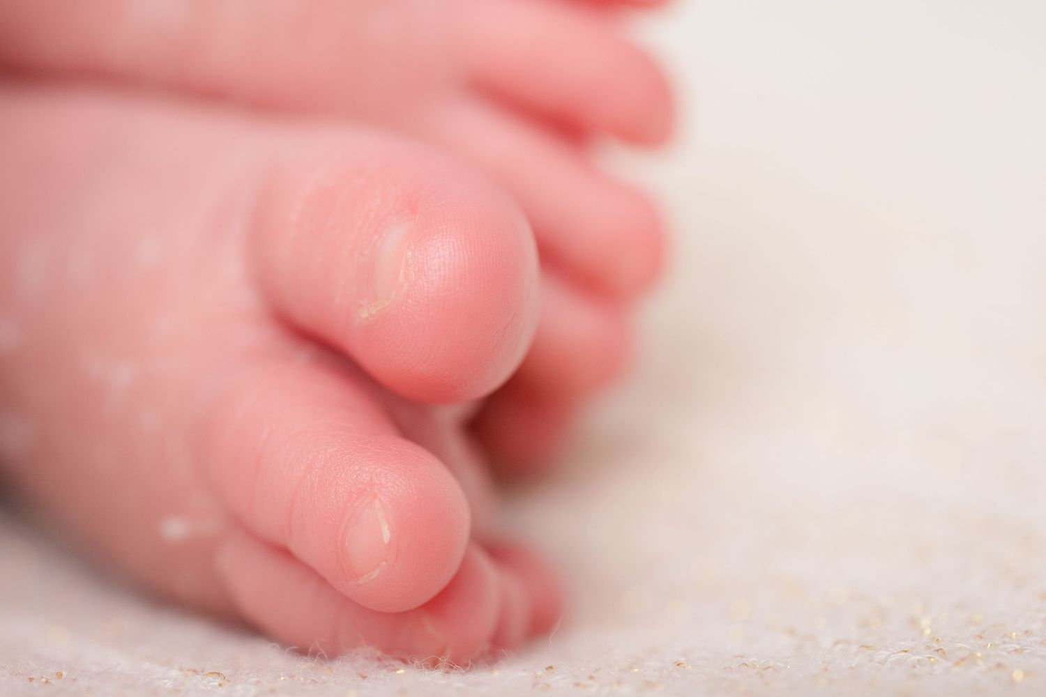 Close-up macro shot of tiny newborn baby toes on white textured fabric.