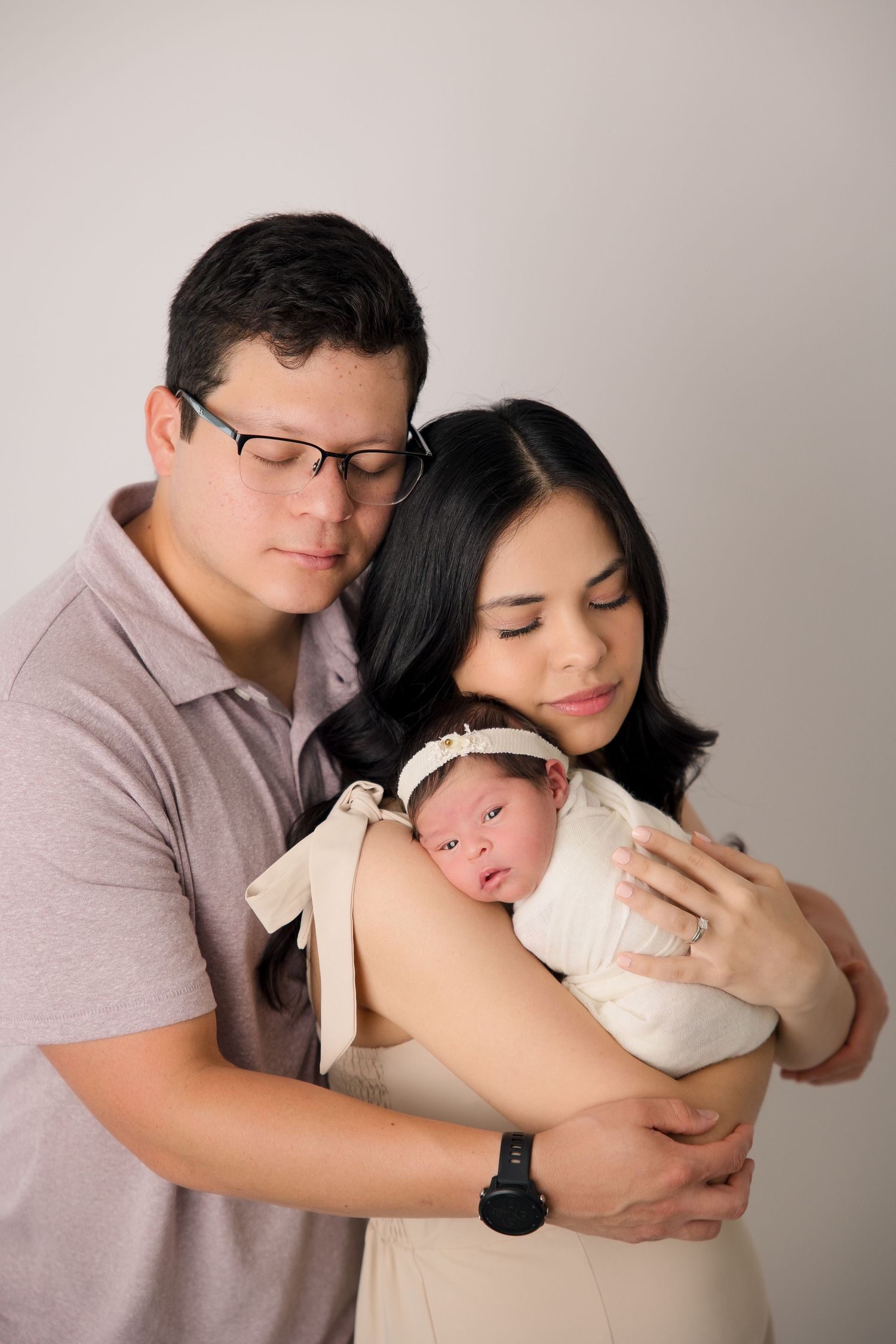 Parents sharing an intimate moment with their newborn baby wrapped in cream fabric.