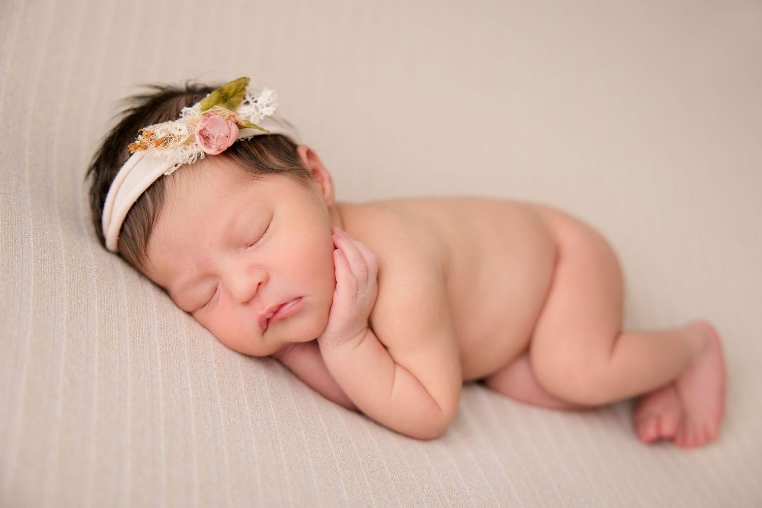 Sleeping newborn baby wearing floral headband lying on soft cream colored blanket.