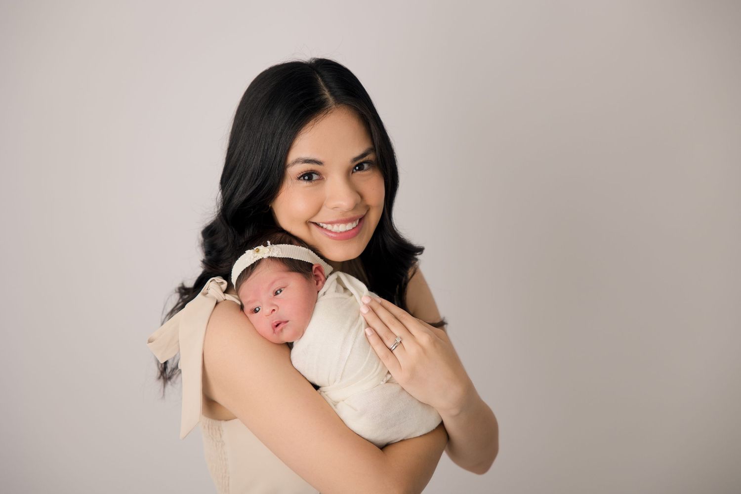 A tender moment captured between parent and newborn baby wrapped in white against a neutral backdrop.