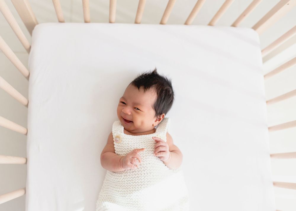 Newborn baby laughing while lying in her cot.