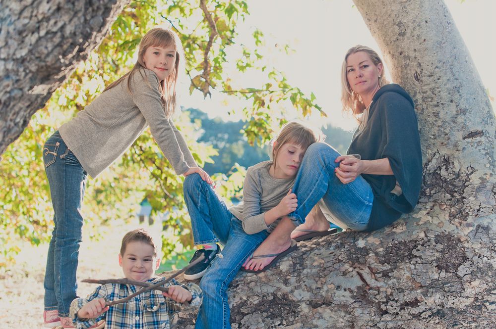 Mother and three children playing and relaxing on a large tree branch outdoors.