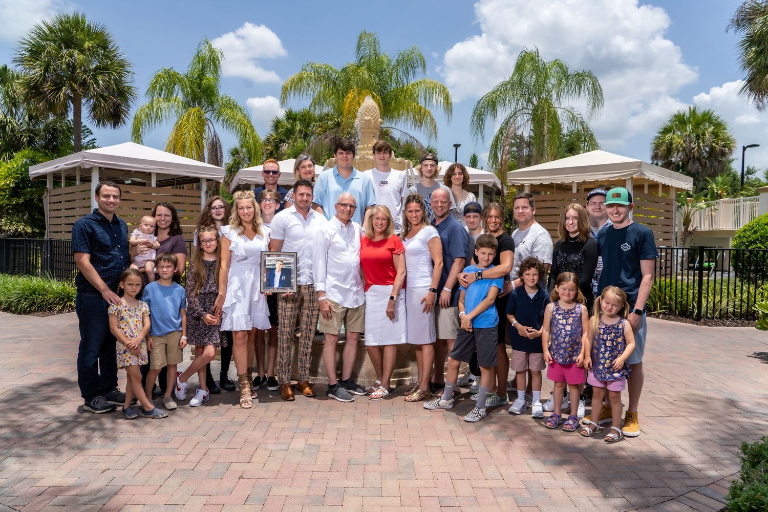 Extended family gathering poses for group photo in front of palm trees.
