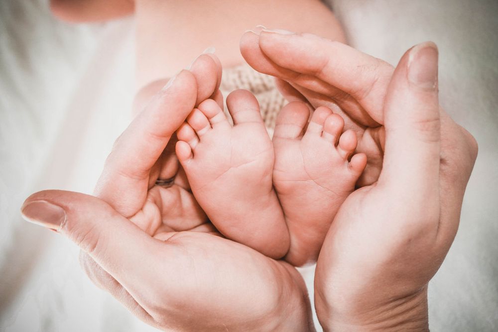 Baby's tiny feet cradled gently in adult hands creating a heart shape.