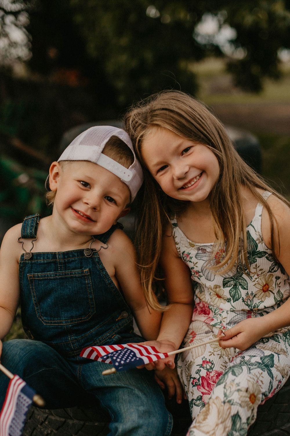 Two children in casual summer outfits sit together sharing a joyful moment outdoors.
