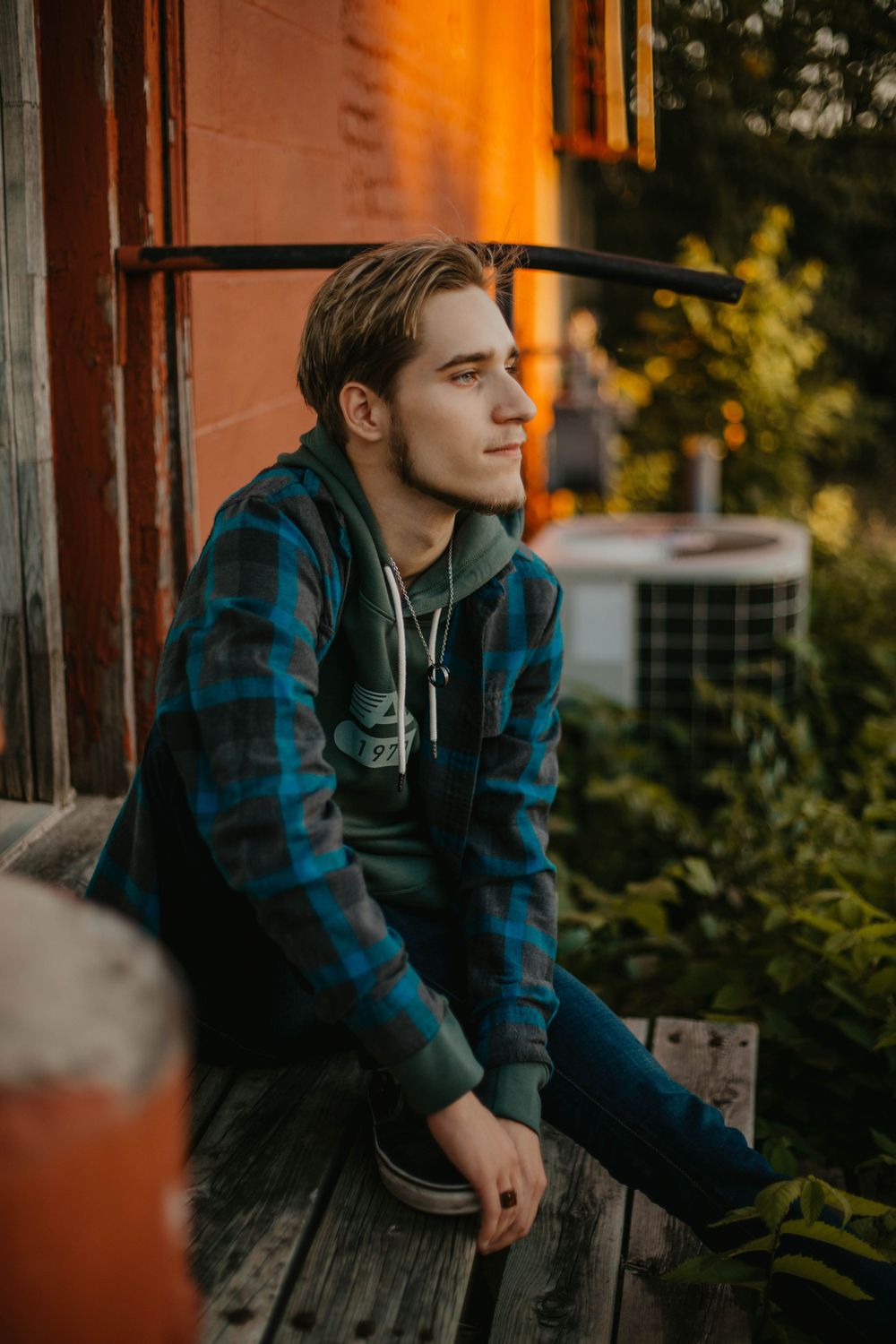 Person in plaid flannel jacket sits on wooden porch during golden hour sunset.