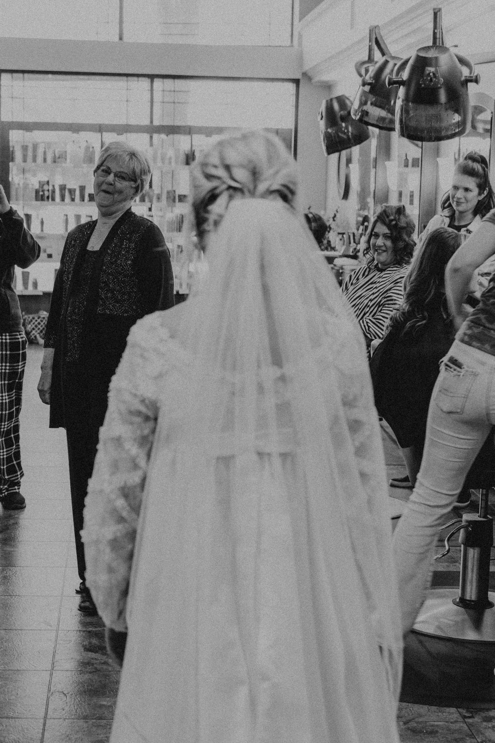 Bride in flowing veil surrounded by people in a bridal salon.