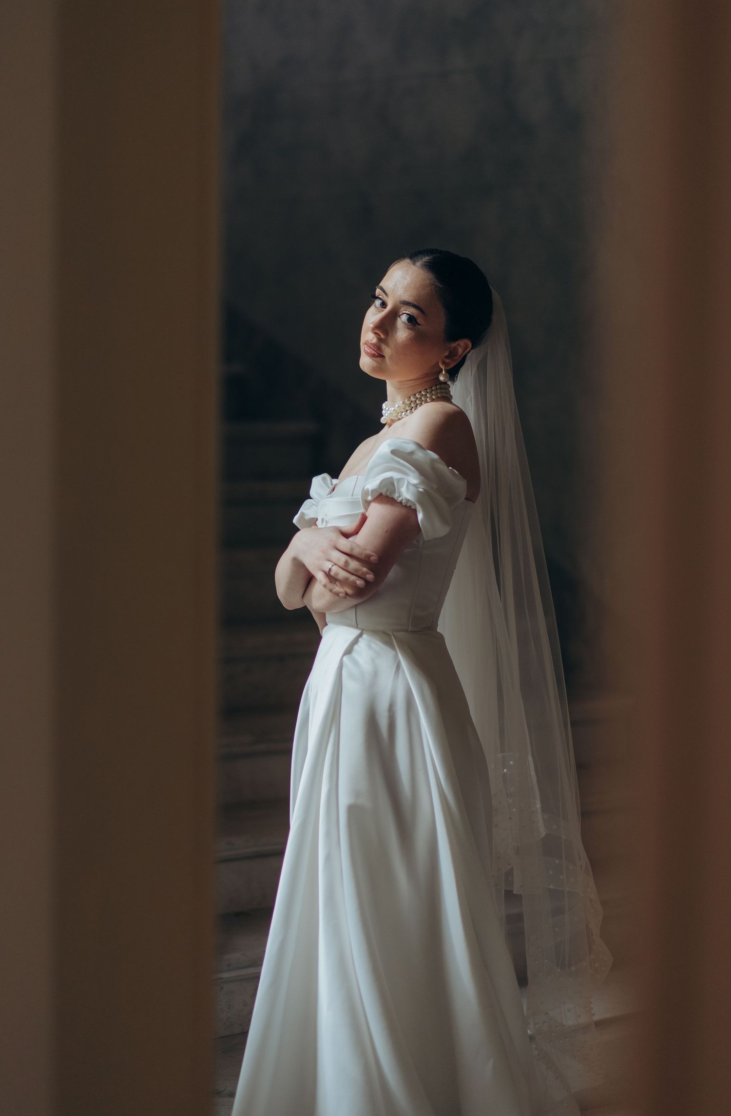 A graceful figure in a classic white wedding gown poses elegantly near a window.