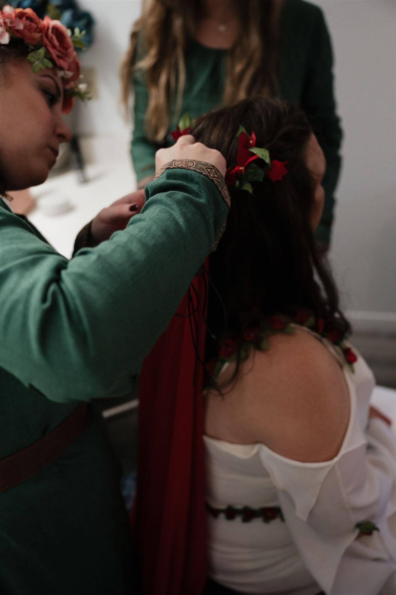 Someone in a green dress adjusts flowers and decorative elements in another person's hair.