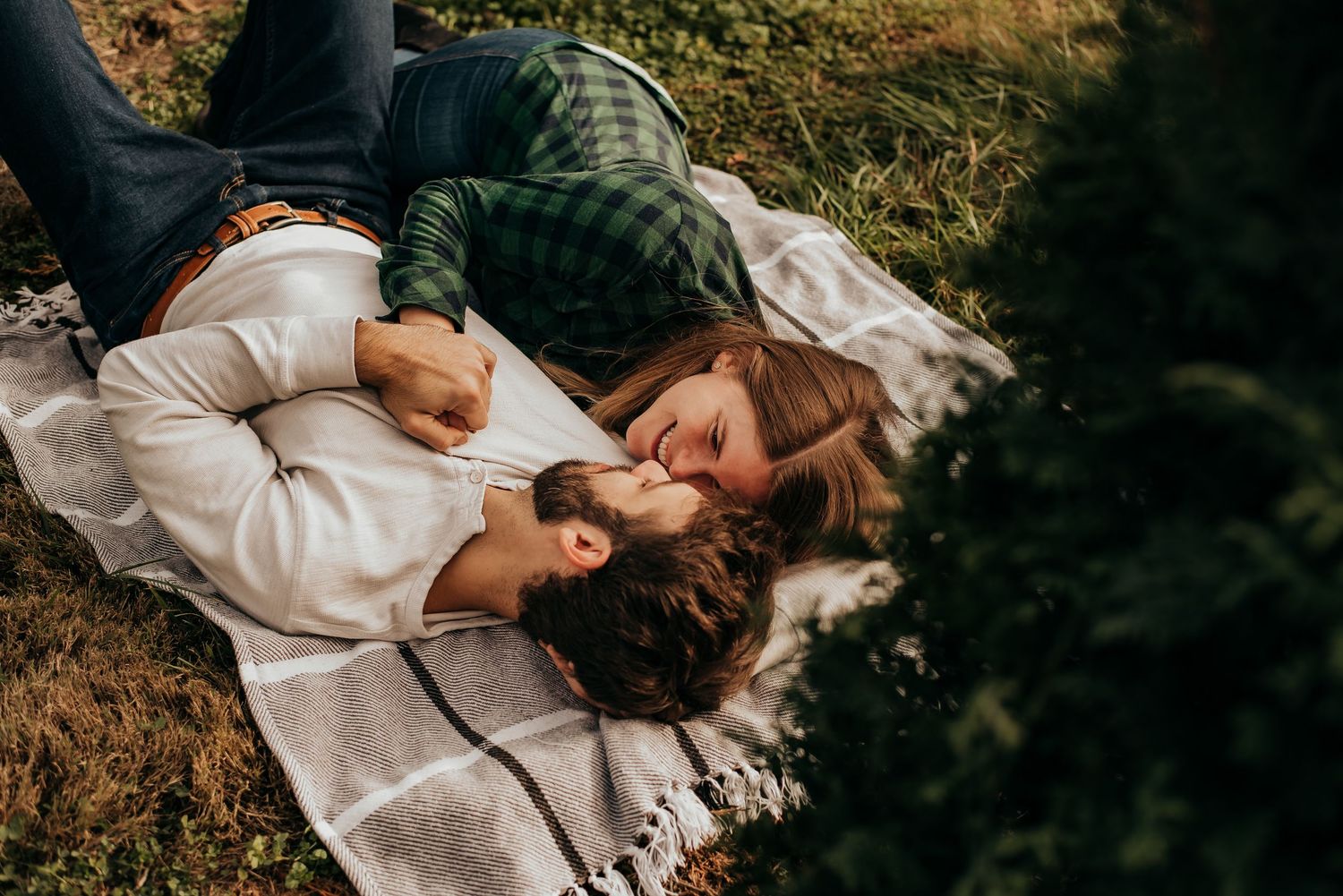 Young couple lies on a blanket in a meadow, sharing a tender romantic moment outdoors.