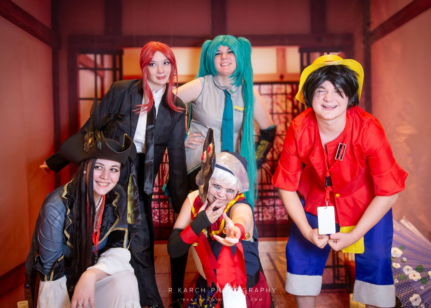 Group cosplay photo featuring five characters in colorful outfits posing together indoors.