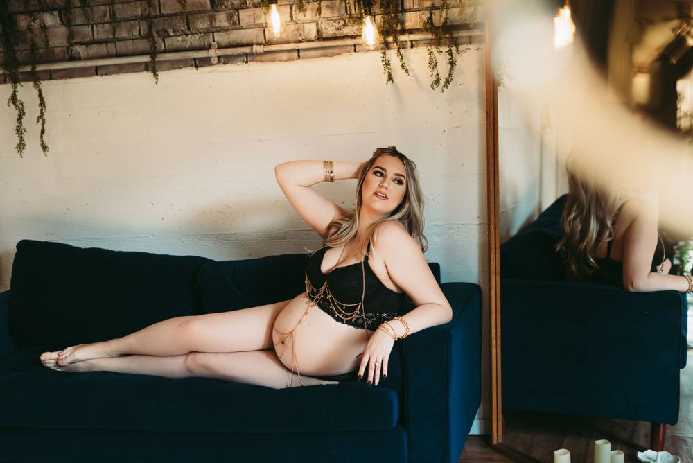A boudoir photography session on a navy blue couch in moody indoor lighting.