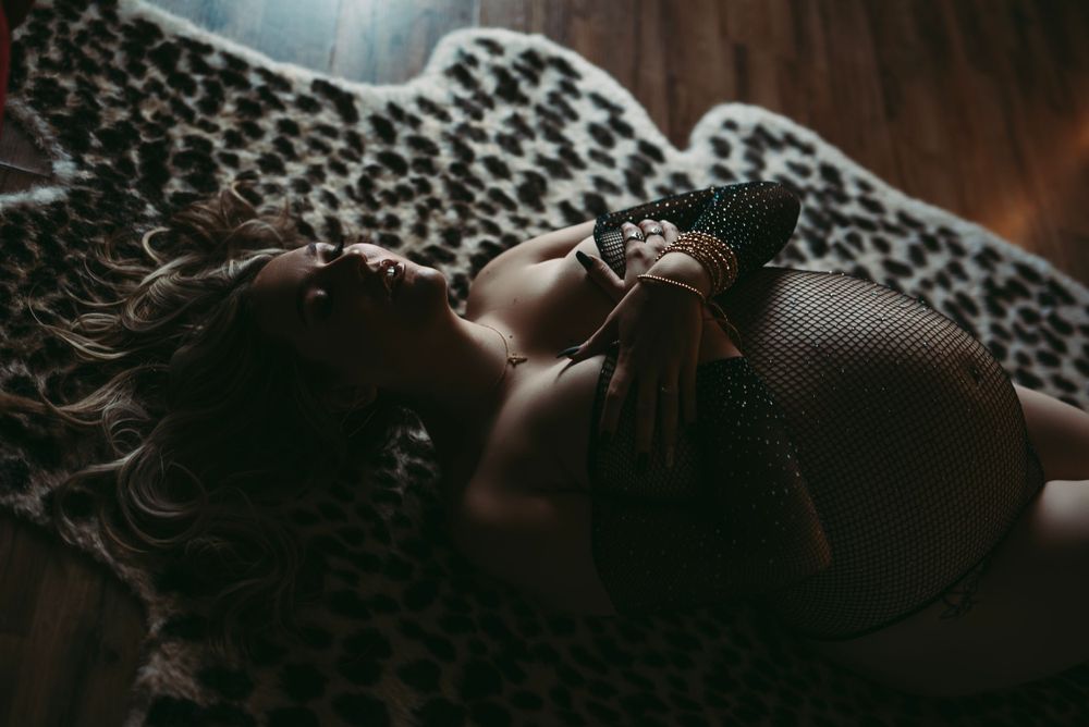 A figure lounges on an animal print fabric in moody dramatic lighting creating an intimate artistic portrait.