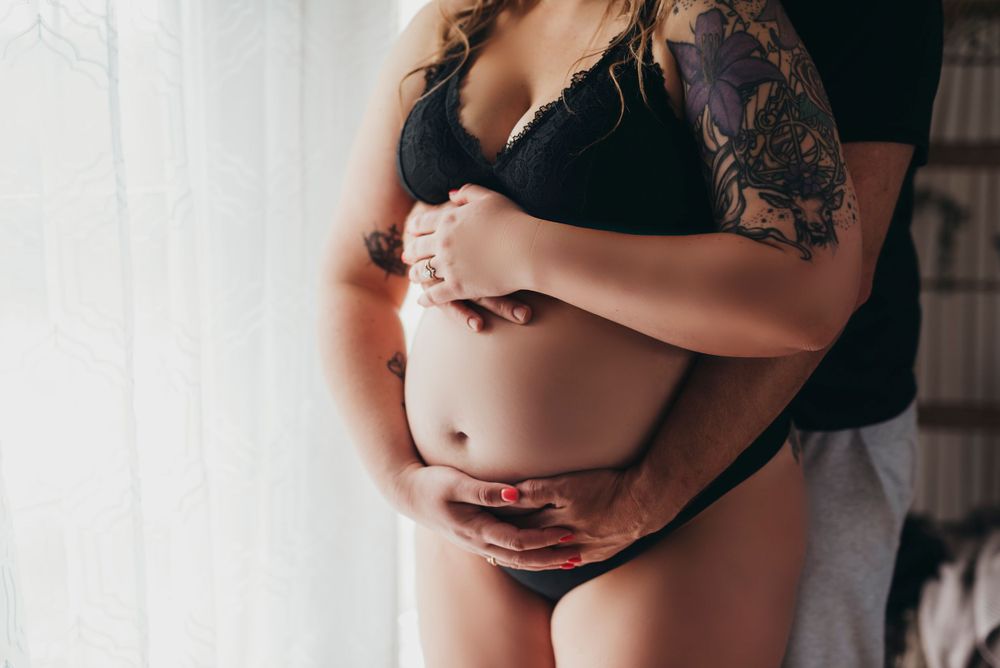 Artistic maternity photograph showing pregnant belly with tattoo detail against soft natural lighting.
