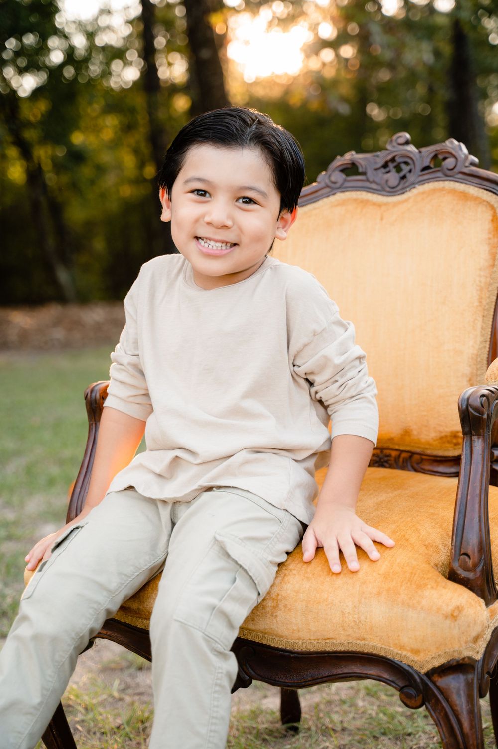 Young child sits on vintage golden chair outdoors during sunset portrait session.