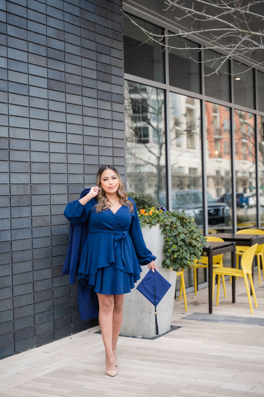 Woman in flowing blue dress poses confidently against modern urban backdrop with matching purse.